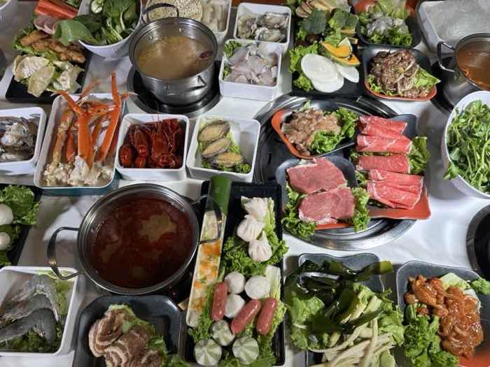 Korean BBQ and hot pot together at Hot Lava Pot Overhead view of a full table with red and clear broths, snow crab legs, sliced beef, pork belly and seafood around a central grill