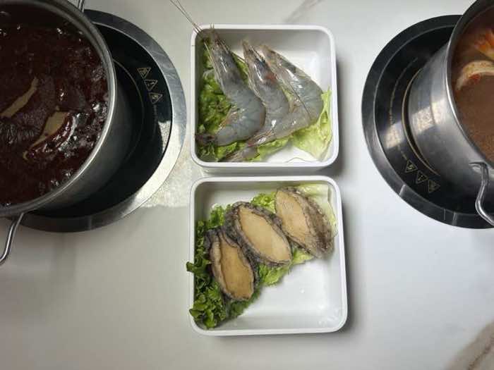 Prawns and abalone beside two broths Fresh head-on prawns and abalone plated between a spicy red broth and a second simmering pot